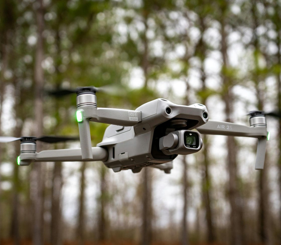Close-up of a drone in midair with trees in the background, showcasing technology and nature.