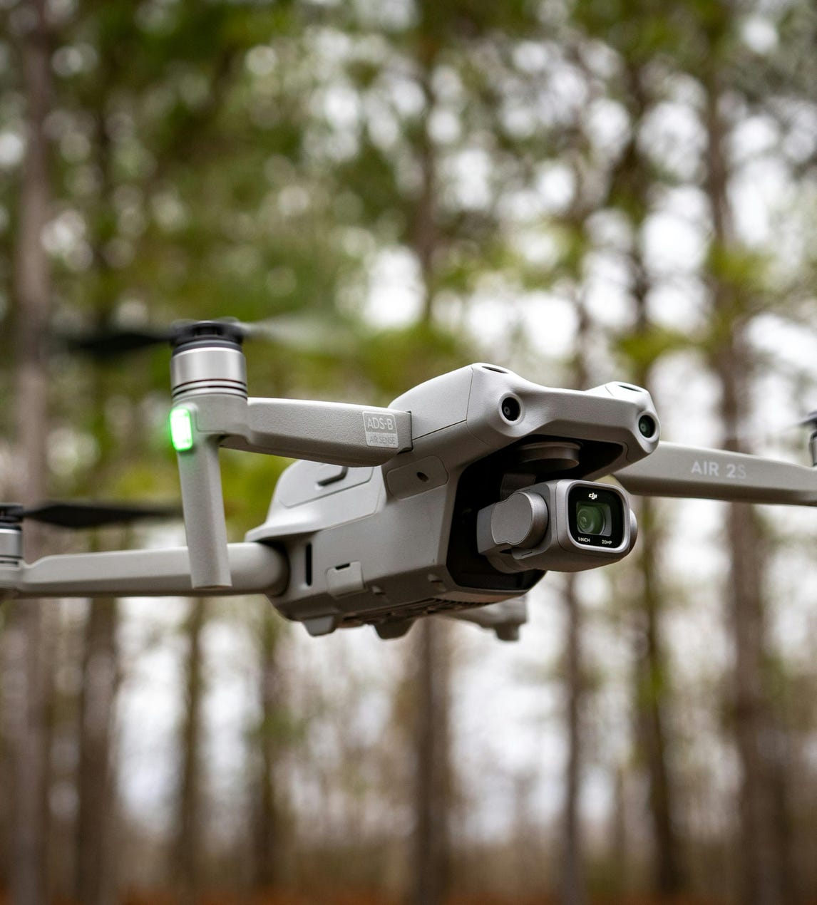 Close-up of a drone in midair with trees in the background, showcasing technology and nature.