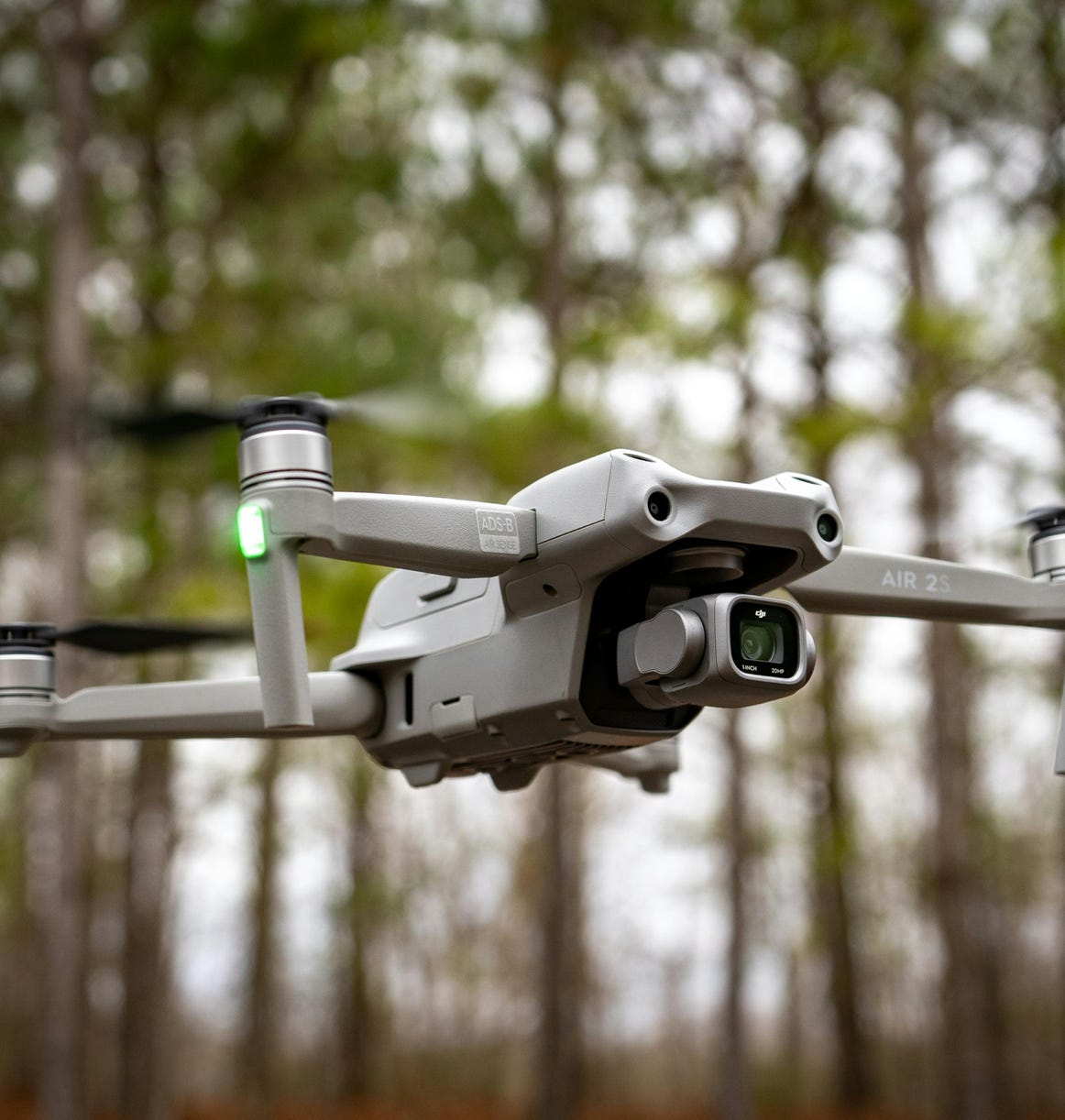 Close-up of a drone in midair with trees in the background, showcasing technology and nature.